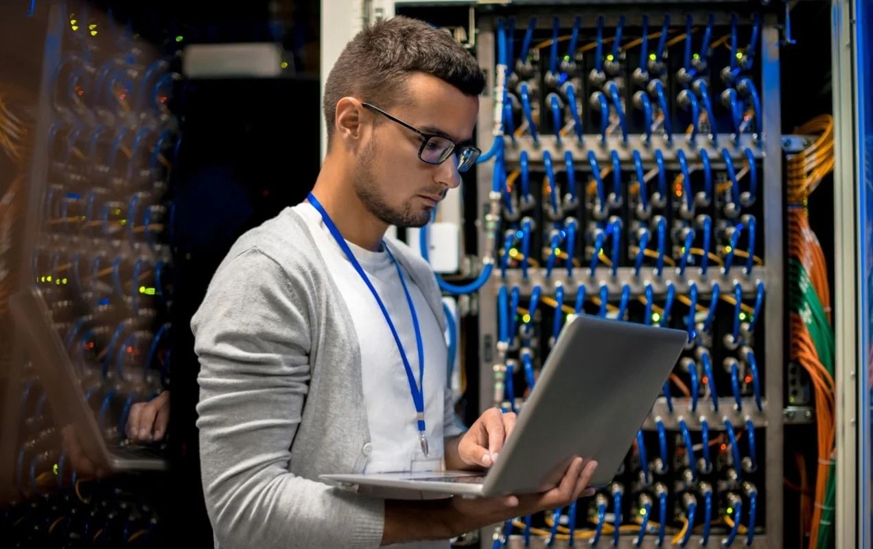 man working in a server room on a laptop