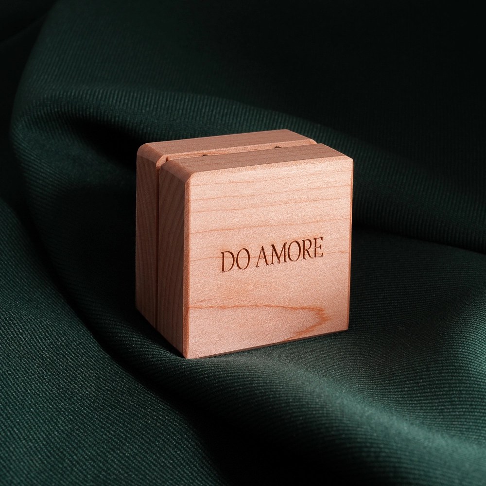 A wooden ring box that reads "Do Amore", placed on a dark green cloth background